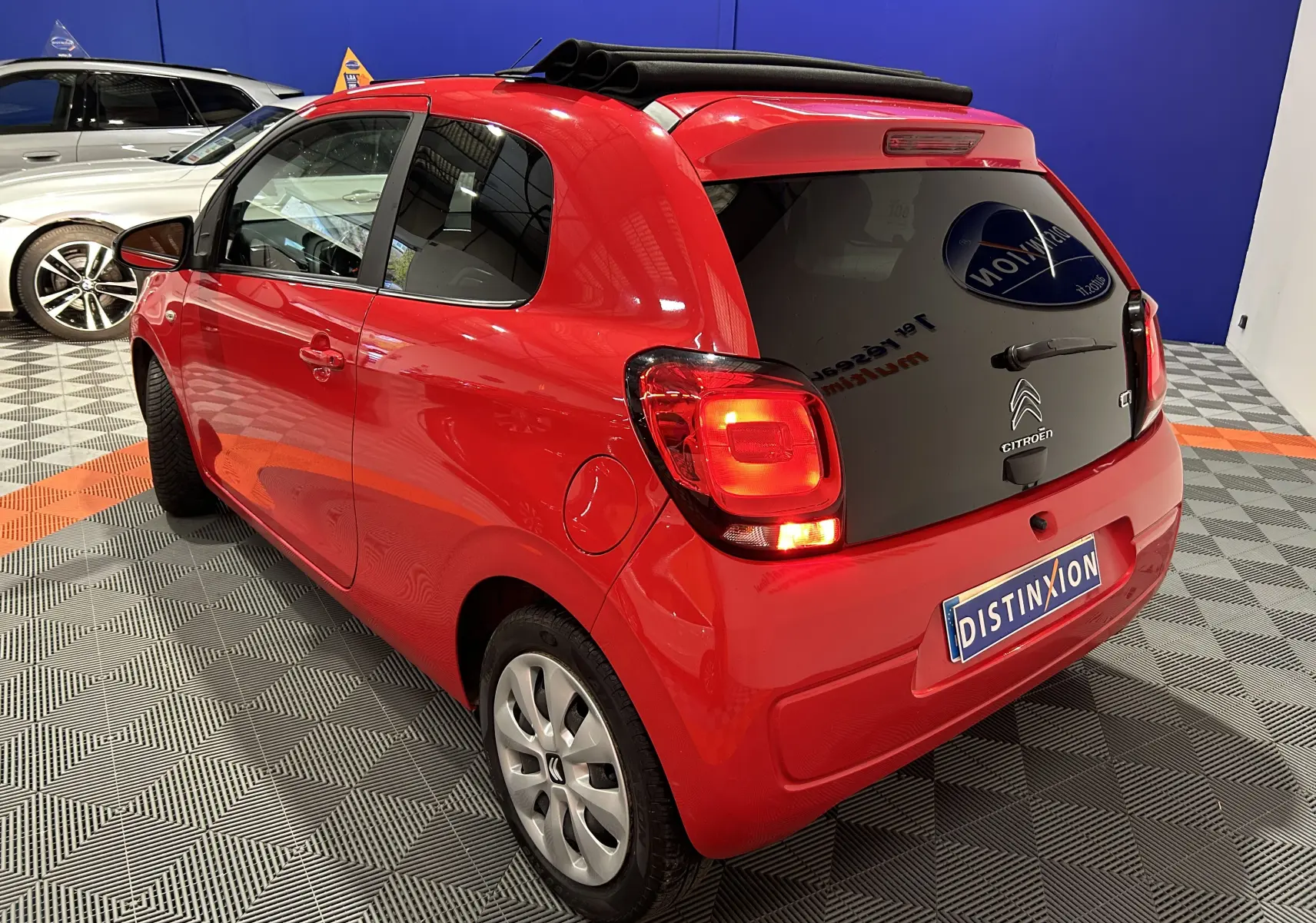 Vue 3/4 arrière droite d'une Citroën C1 rouge 3 portes avec toit ouvrant replié et feux arrière allumés.