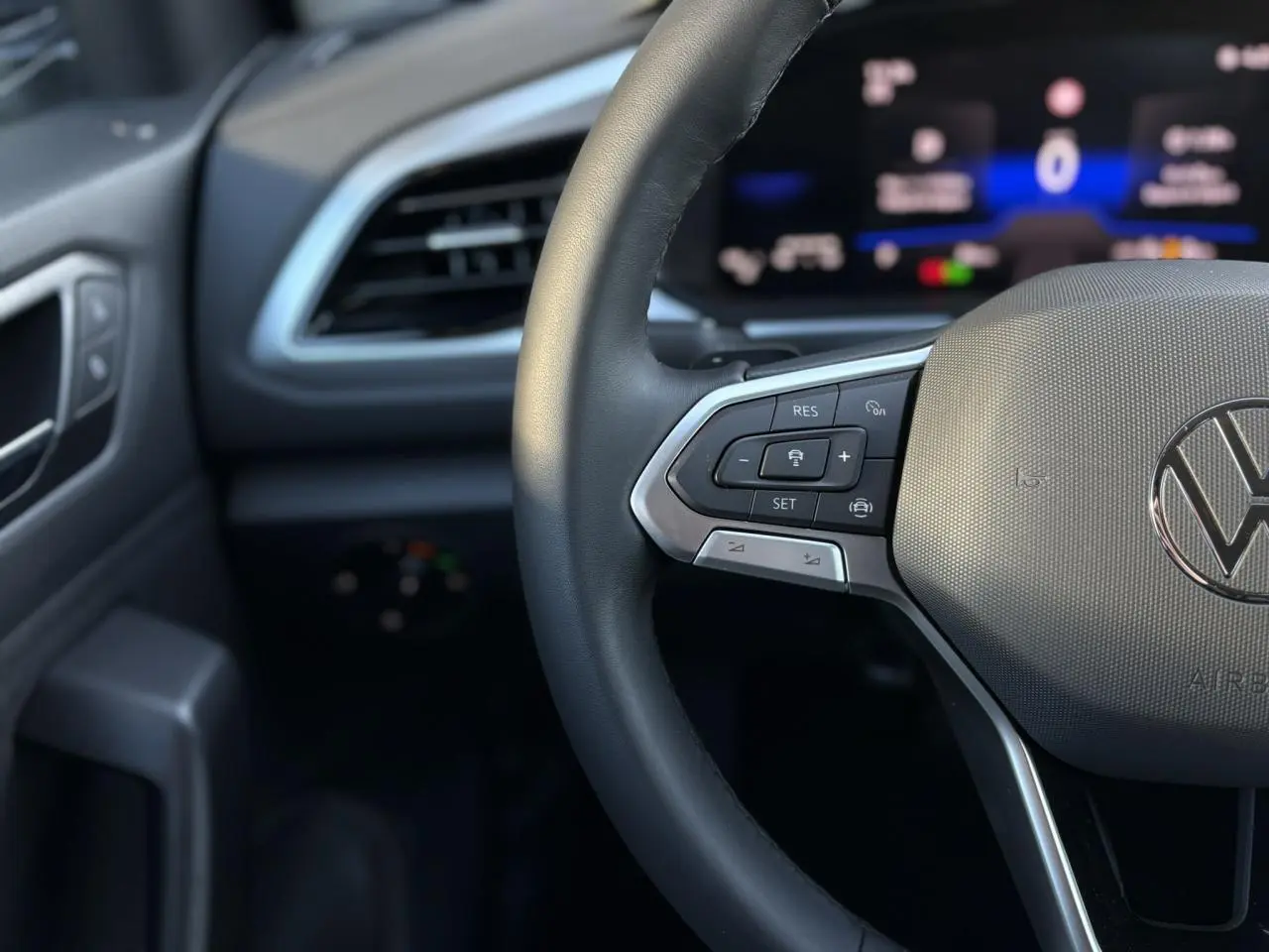 Gros plan sur le volant cuir multifonction du Volkswagen T-Roc 1.5 TSI argent avec tableau de bord digital flou en arrière-plan.