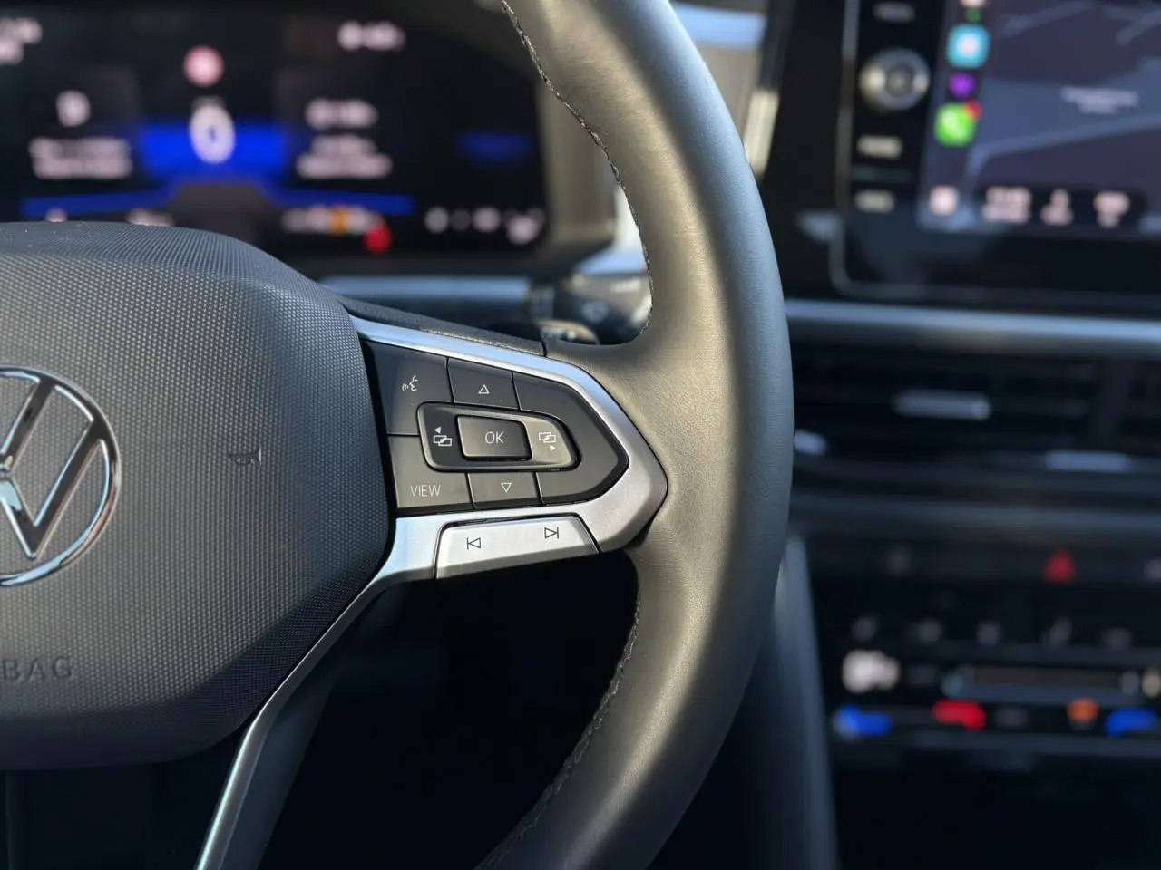 Gros plan sur le volant multifonction en cuir noir du Volkswagen T-Roc 2025 avec écran digital flou en arrière-plan.