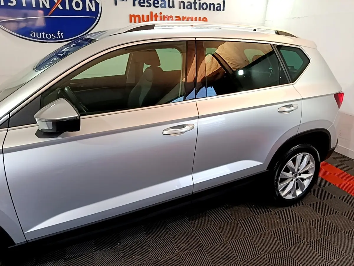 Vue de profil côté gauche du SEAT Ateca gris clair 2022 avec jantes alliage et barres de toit chromées.