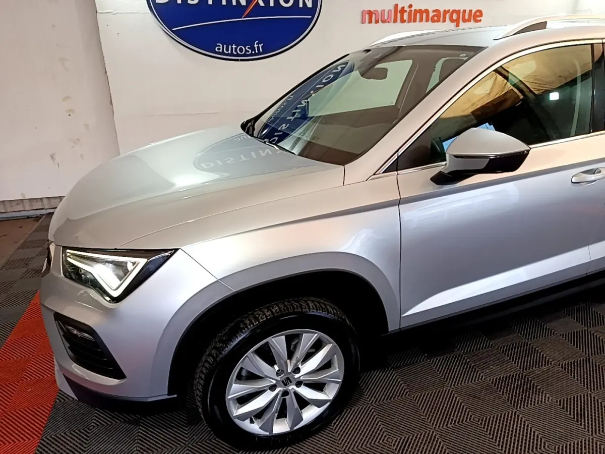 Vue de profil avant droit d’un SEAT Ateca gris clair avec jante alliage et feux LED allumés en intérieur showroom.