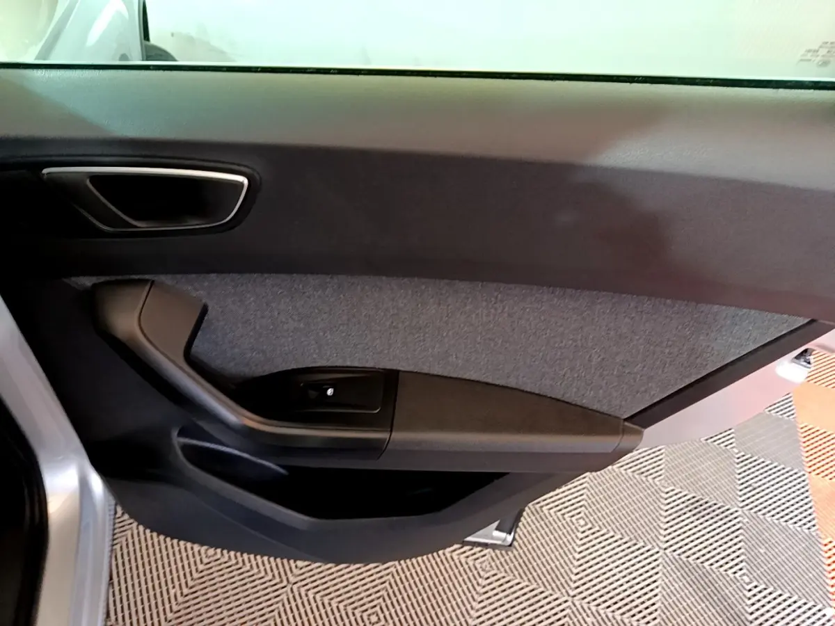Vue intérieure de la porte côté gauche d’un SEAT Ateca gris clair, avec poignée noire et garniture textile grise.