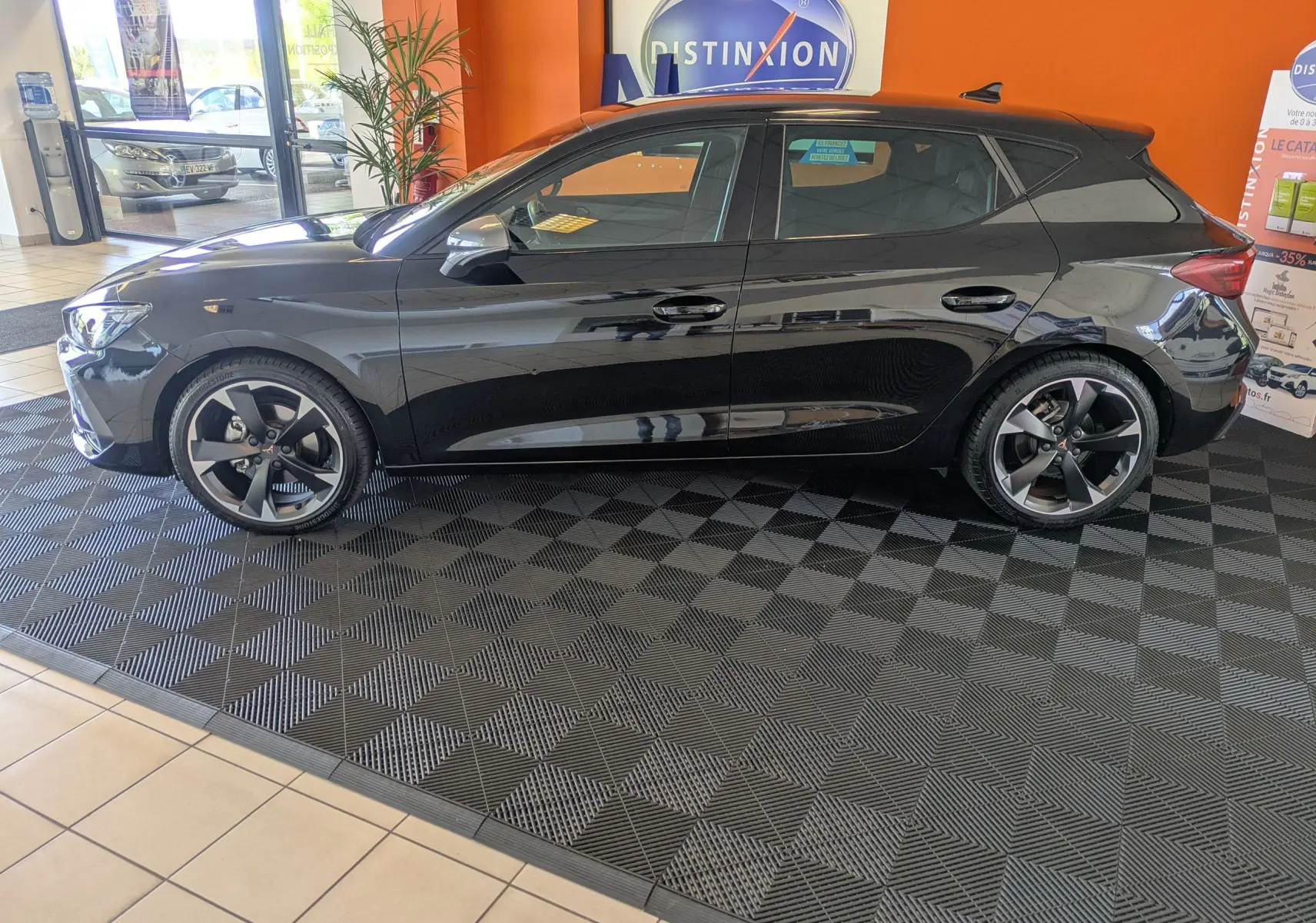 Profil droit d'une CUPRA Leon noire 2025 en intérieur, avec jantes alliage 18 pouces bicolores et vitres teintées.