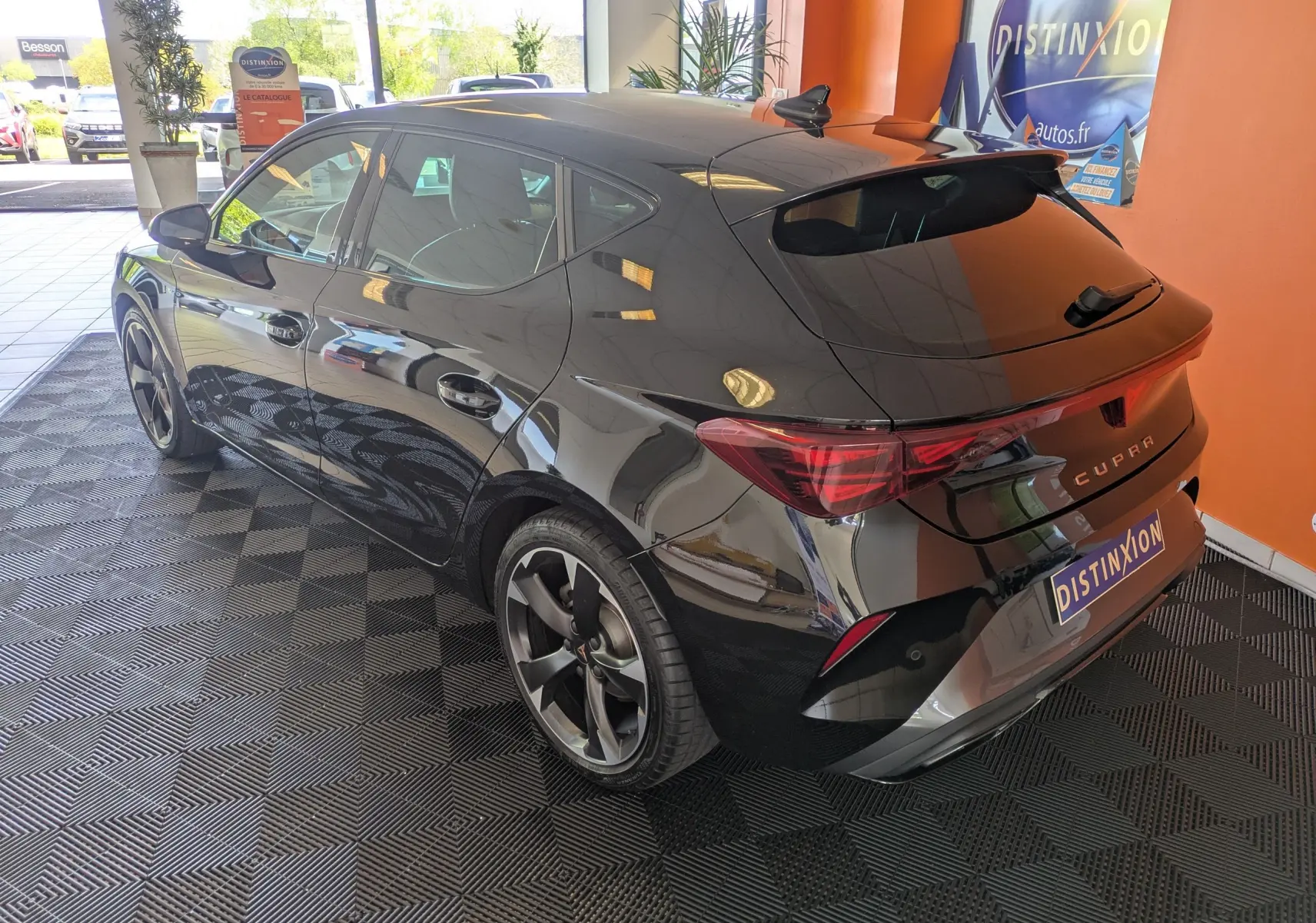 Vue 3/4 arrière droite d'une CUPRA Leon noire 2025 avec jantes alliage 18 pouces bicolores et vitres teintées, en intérieur showroom.