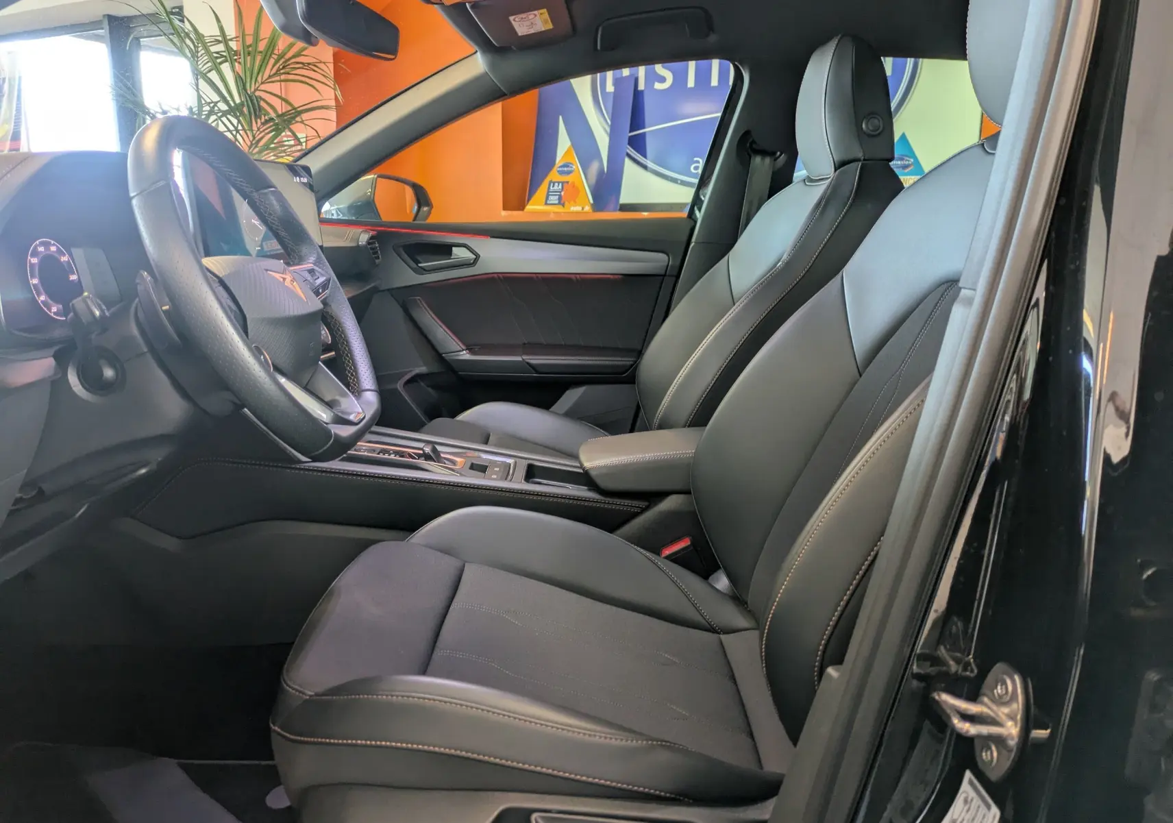 Vue intérieure côté conducteur de la CUPRA Leon 2.0TDI 150 DSG7 noire, avec sièges mix cuir tissu et volant multifonction.