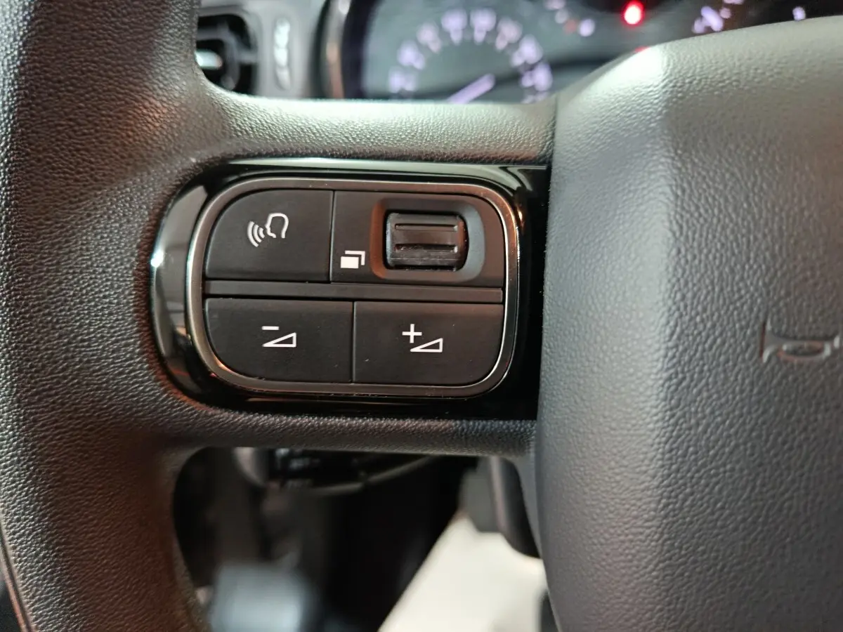 Gros plan sur les commandes multifonctions noires du volant de la Citroën C3 2024, intérieur gris foncé.
