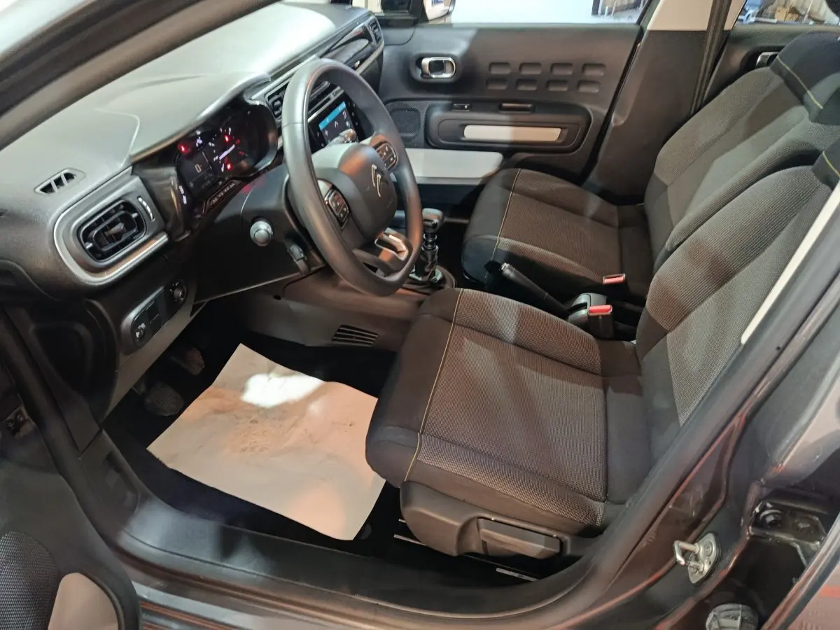 Vue intérieure côté conducteur de la Citroën C3 gris foncé 2024, montrant sièges tissu et tableau de bord avec volant multifonctions.