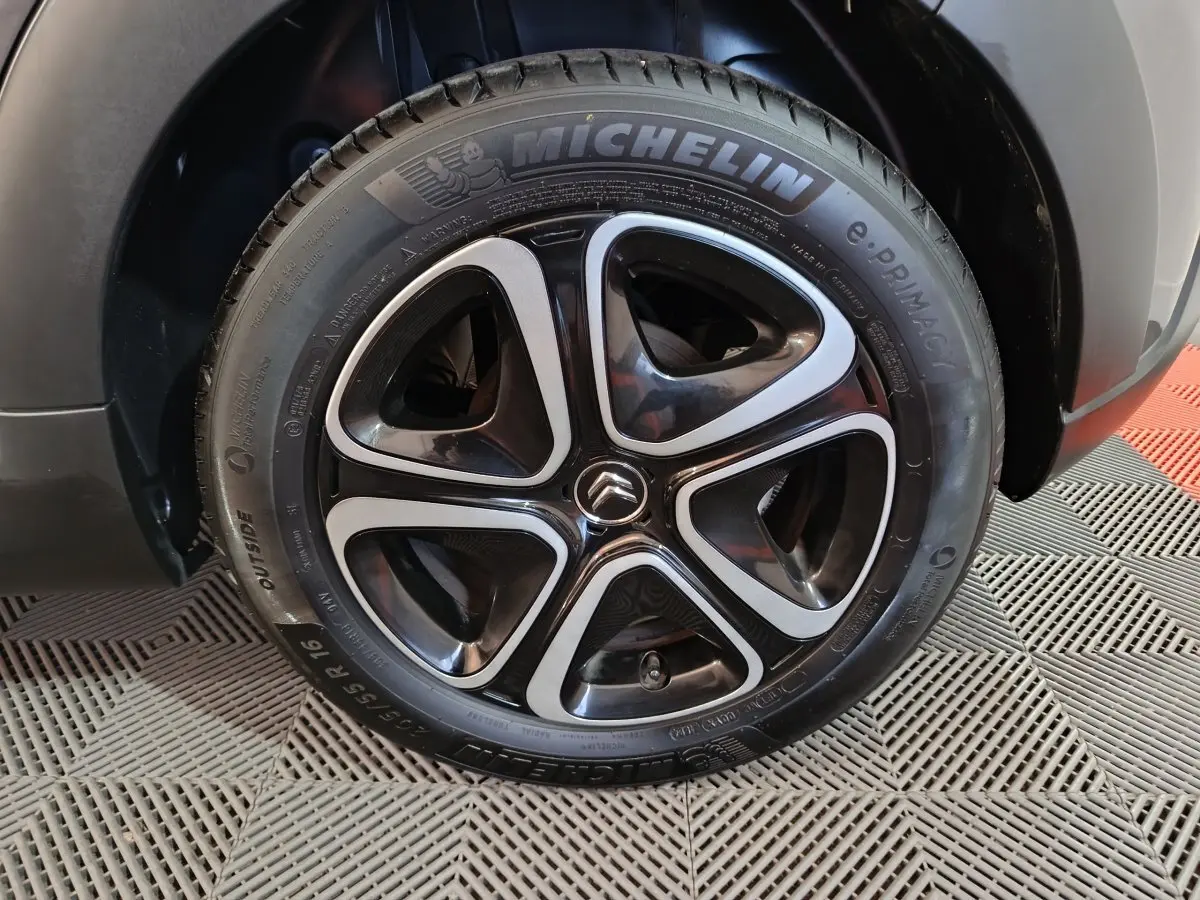Gros plan sur la roue avant droite d'une Citroën C3 gris foncé, avec jante noire et inserts argentés distinctifs.
