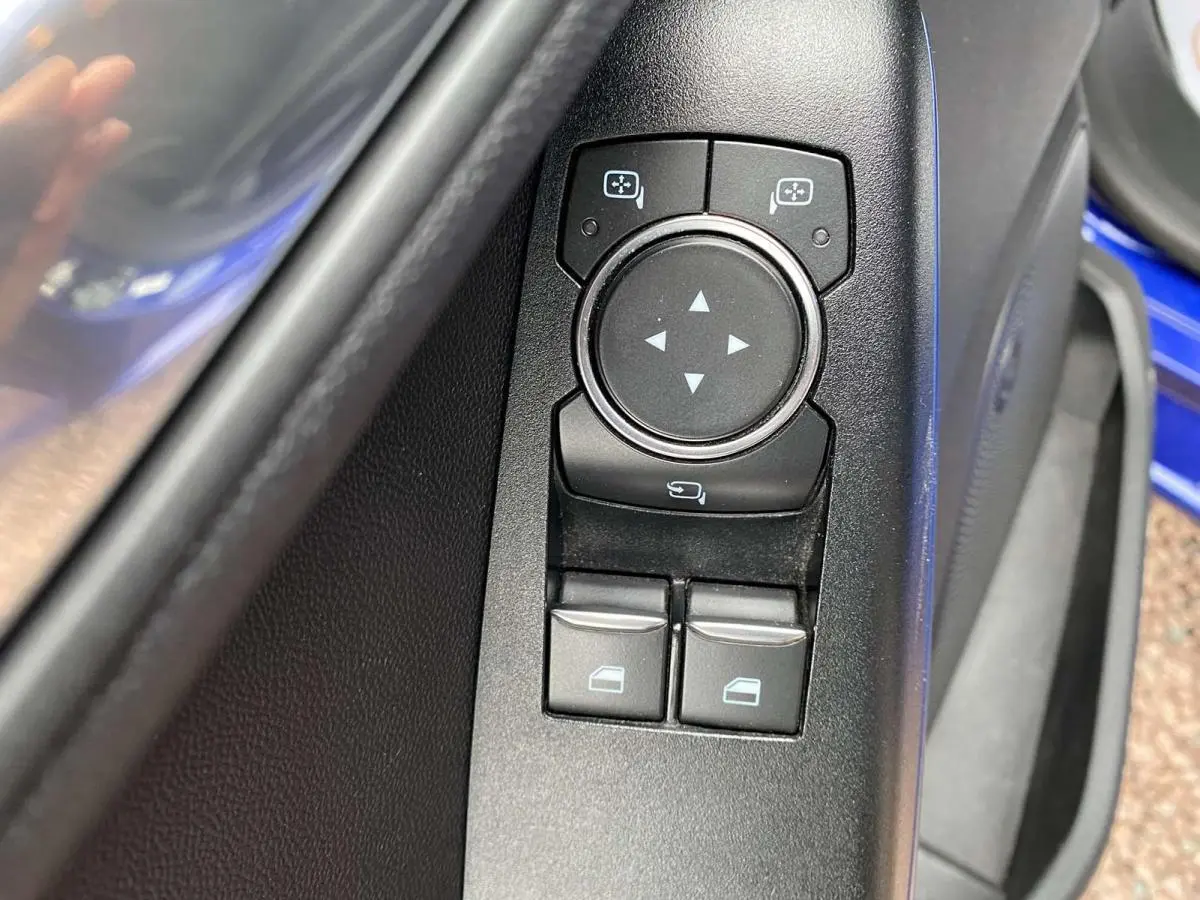 Gros plan sur les commandes de réglage des rétroviseurs et des vitres côté conducteur d'une Ford Fiesta bleu foncé 2017.
