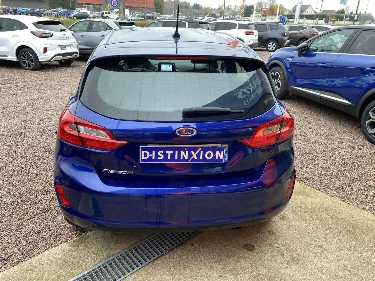 Vue arrière d'une Ford Fiesta bleu foncé 2017 avec plaque Distinxion, stationnée sur sol gravillonné.