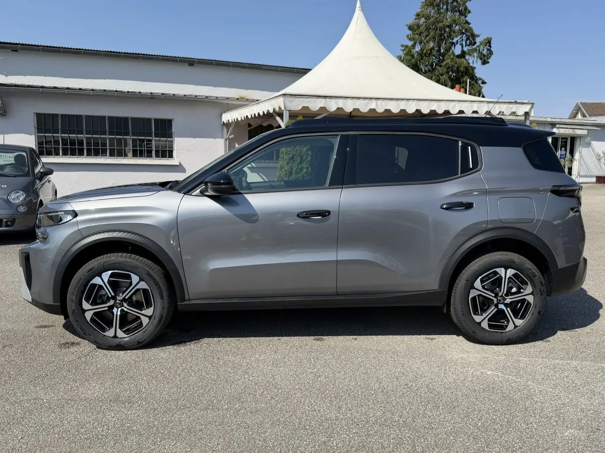 Vue de profil côté gauche d'un Citroën C3 Aircross gris clair avec toit noir et jantes distinctives.