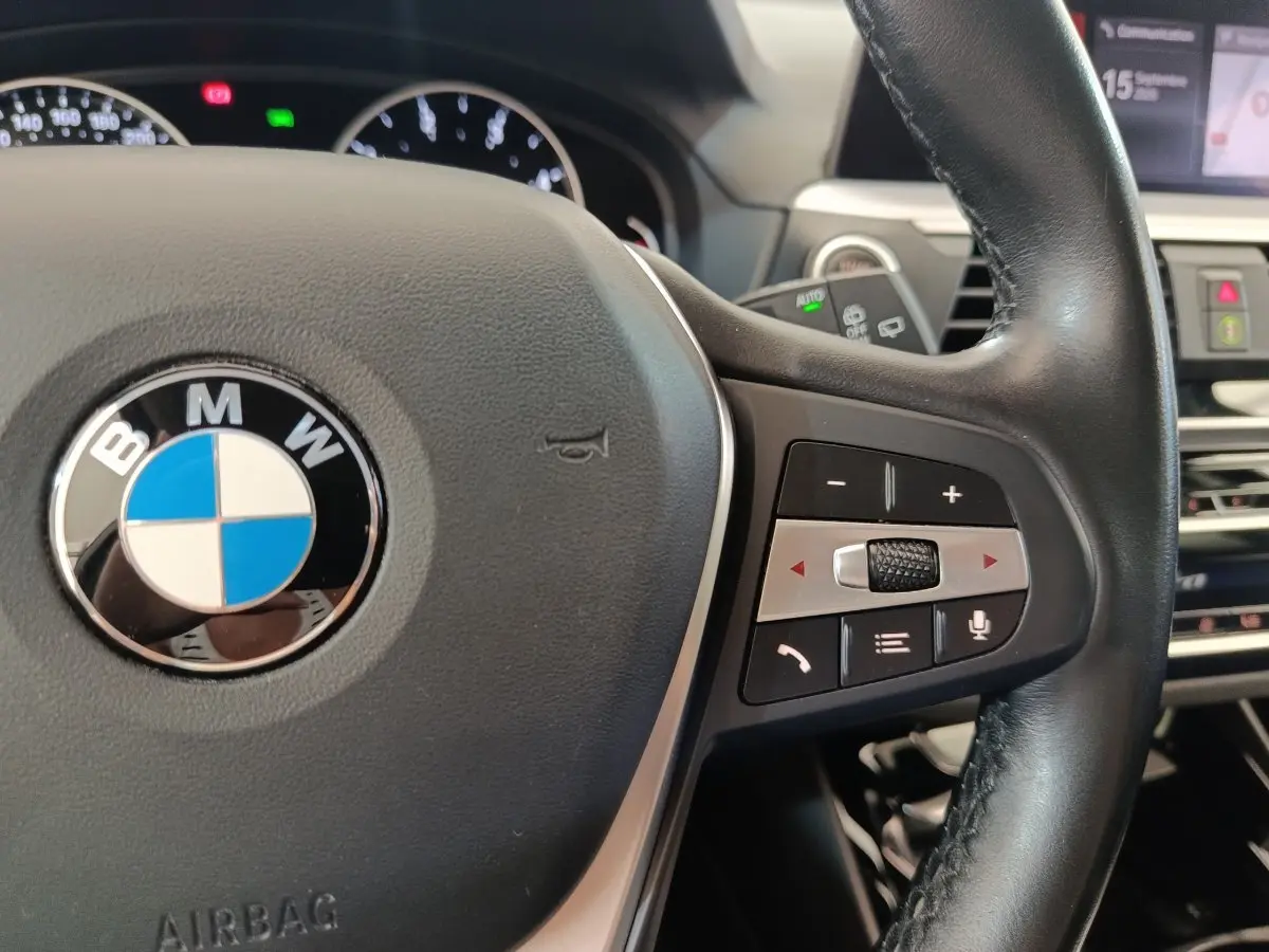 Gros plan sur le volant cuir et alu multifonctions du BMW X3 gris clair, avec commandes intégrées visibles.