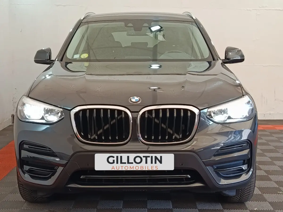 Vue avant d'un BMW X3 gris clair avec calandre double haricot et phares LED allumés en intérieur showroom.