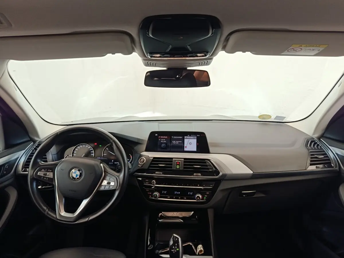 Vue intérieure avant du tableau de bord et volant cuir alu multifonctions d'une BMW X3 xDrive20d gris clair de 2020.