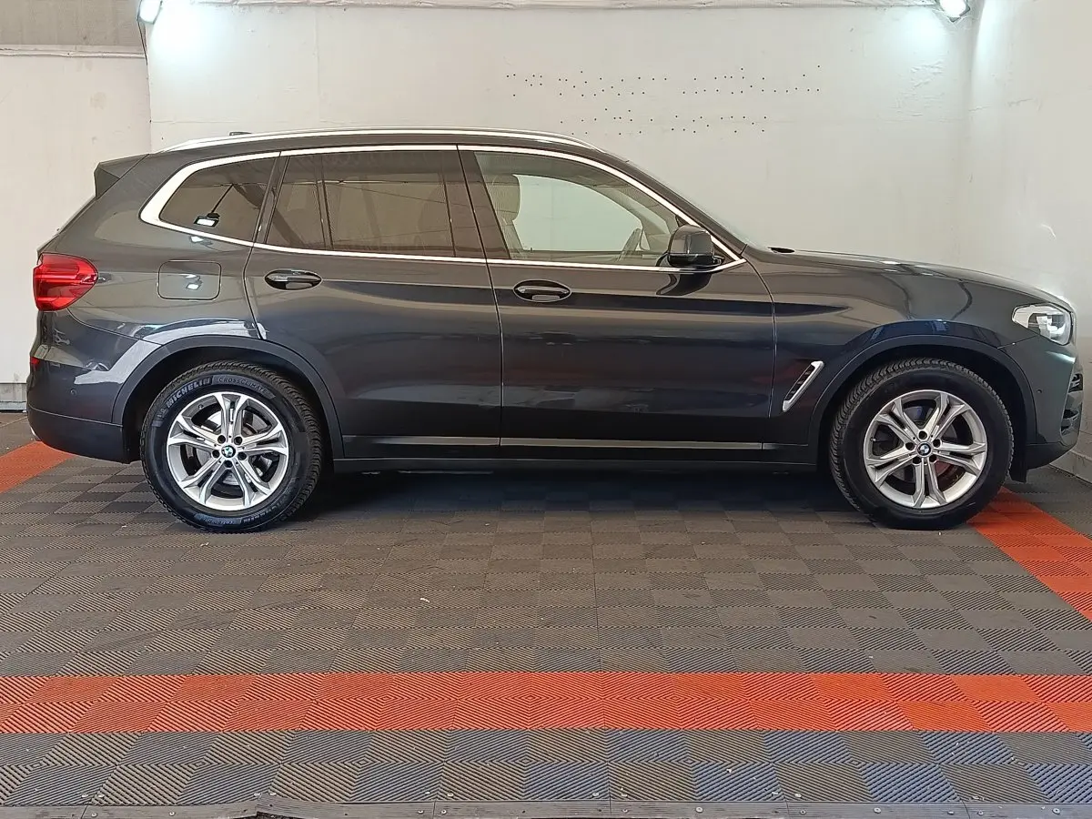 BMW X3 gris clair vue de profil côté gauche dans un garage avec jantes alliage et vitres teintées.