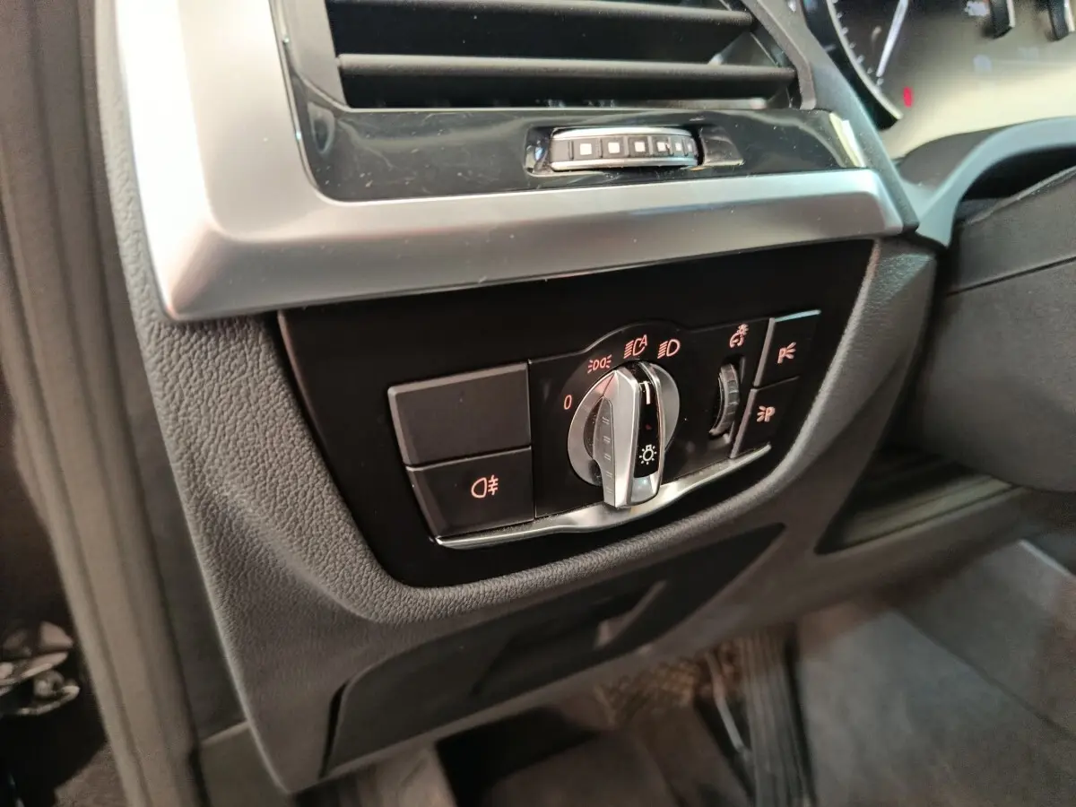 Gros plan sur le panneau de commande des phares à gauche du volant dans l'habitacle gris foncé d'un BMW X3 gris clair.
