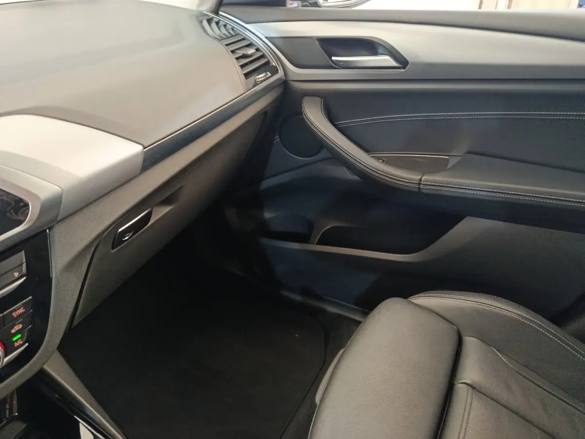 Intérieur côté passager du BMW X3 gris clair 2020, montrant tableau de bord et porte en cuir noir avec surpiqûres.