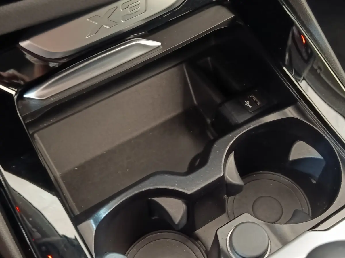 Gros plan sur la console centrale noire du BMW X3 2020 avec porte-gobelets et prise USB, logo X3 visible.