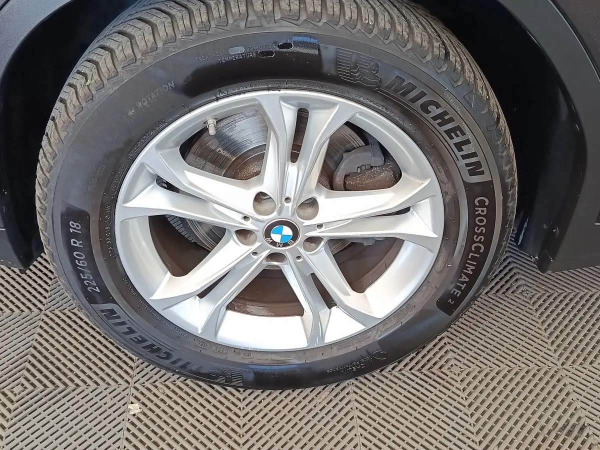 Gros plan sur la roue avant droite d'une BMW X3 gris clair avec jante alliage et pneu Michelin CrossClimate.