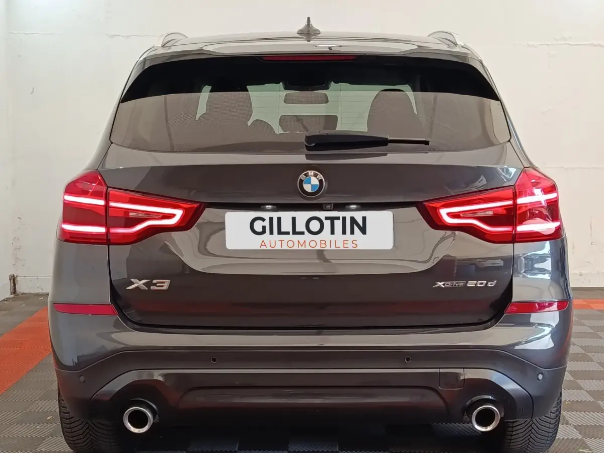 Vue arrière d’un BMW X3 gris clair 2020 avec feux LED allumés et double sortie d’échappement visible.