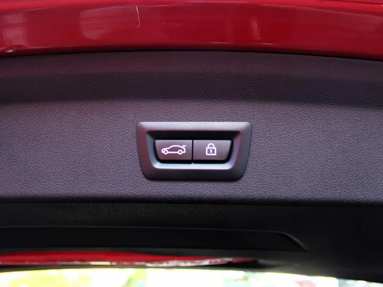 Gros plan sur les boutons d'ouverture et de verrouillage du coffre sur le hayon rouge métallisé d'une BMW Série 1 118d Edition M Sport Pro.