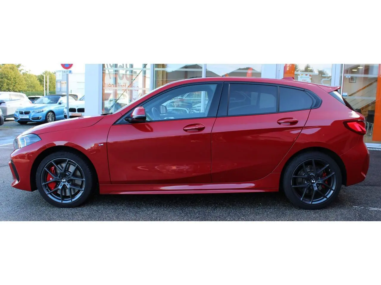 Vue de profil côté gauche d'une BMW Série 1 118d Edition M Sport Pro rouge Melbourne métallisé avec jantes alliage et freins rouges M.
