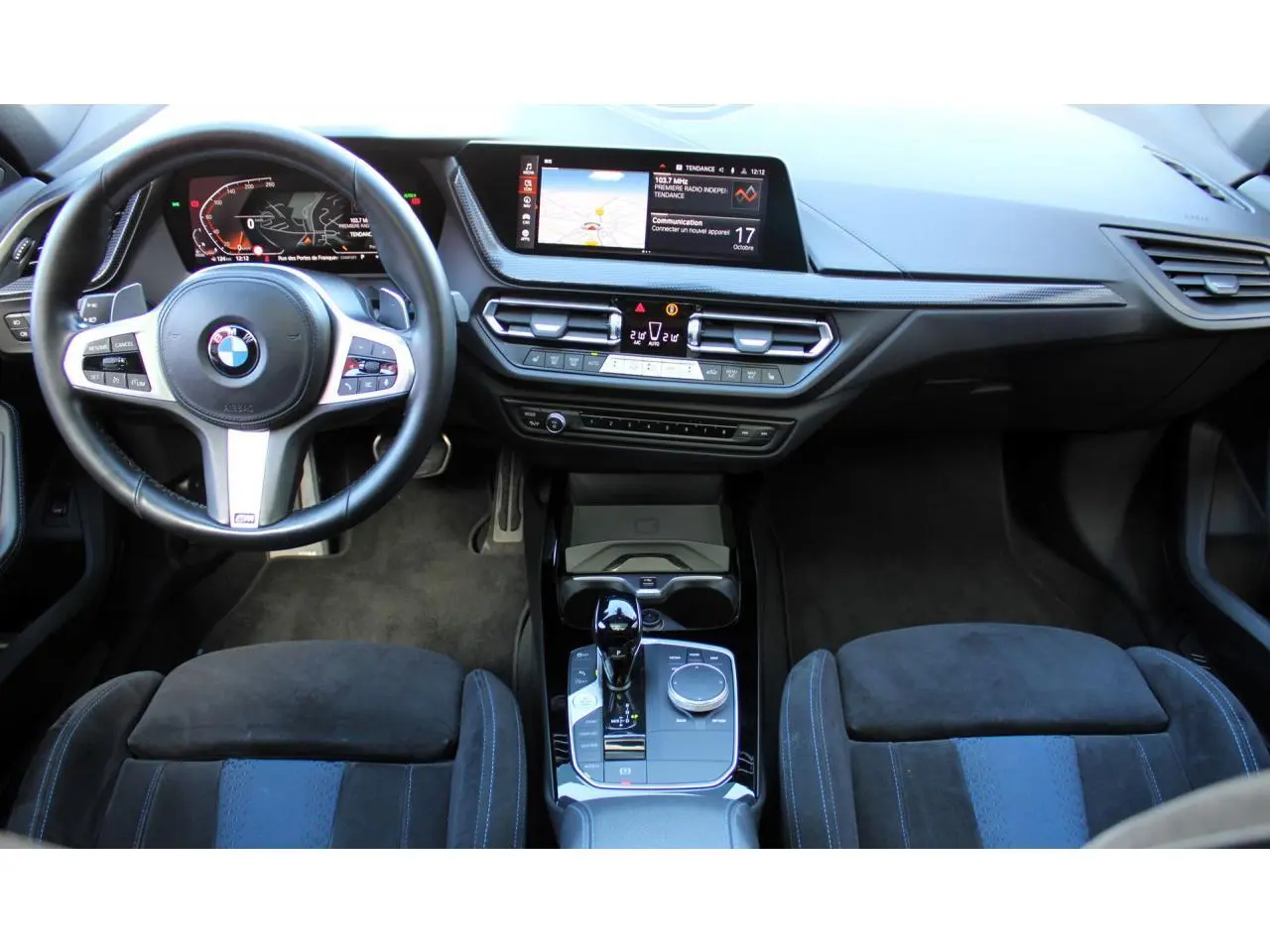 Vue intérieure avant de la BMW Série 1 118d Edition M Sport Pro, tableau de bord moderne avec écran tactile et volant M cuir.