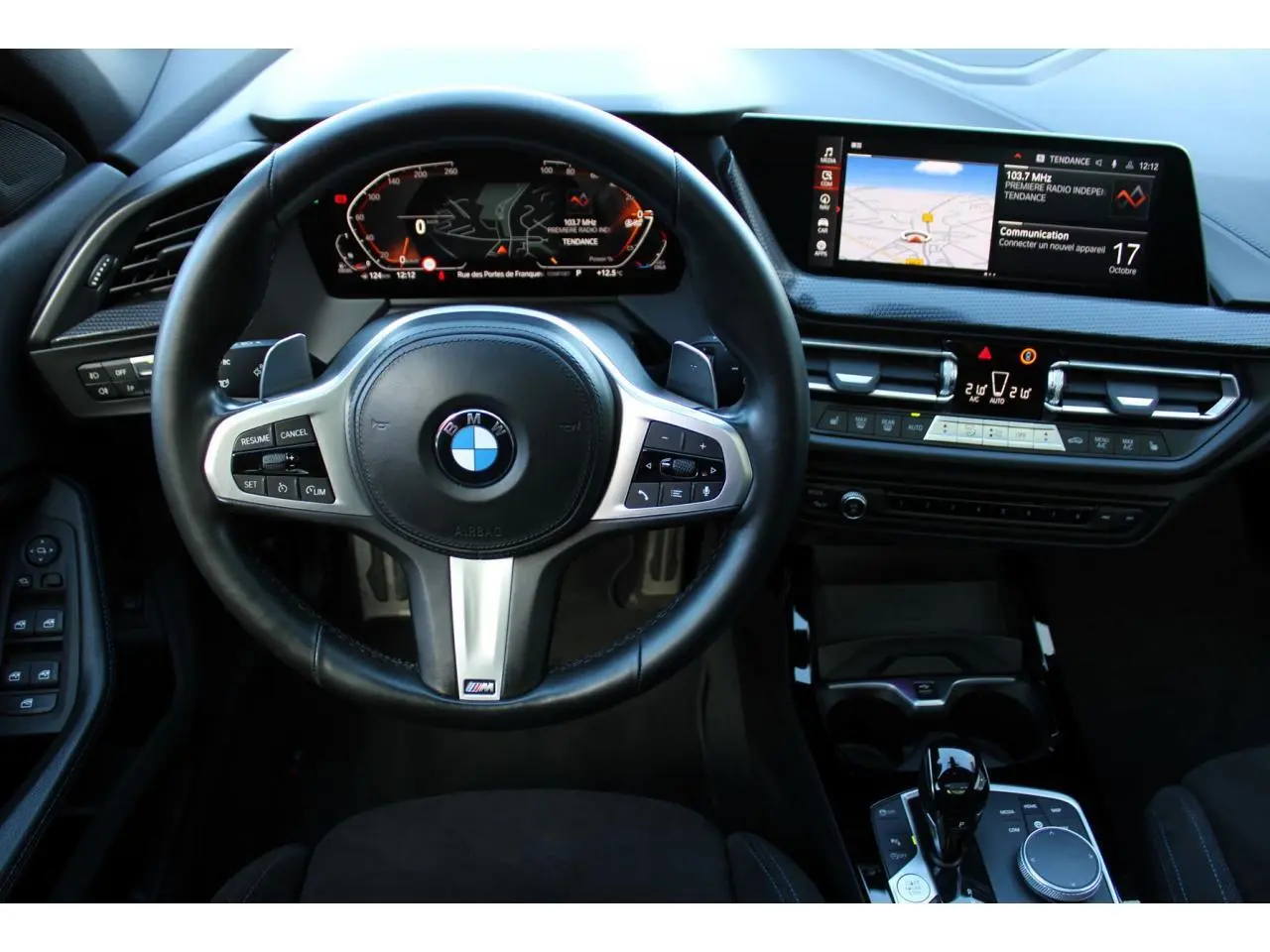Vue intérieure centrée sur le volant M cuir et le tableau de bord numérique de la BMW Série 1 118d Edition M Sport Pro.