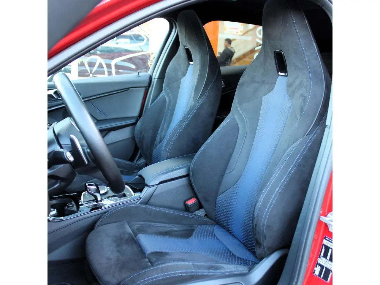 Vue intérieure côté gauche montrant les sièges sport M en tissu Alcantara noir et bleu d'une BMW Série 1 Melbourne Rot.