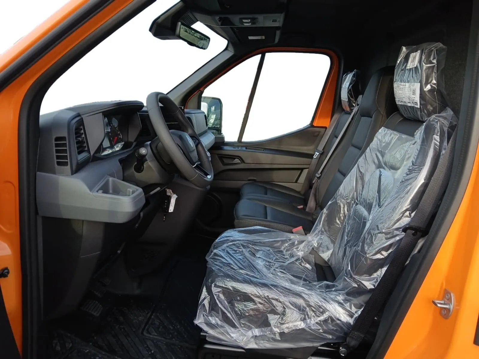Vue intérieure côté conducteur du Renault Master orange 2026, montrant le volant, tableau de bord et sièges protégés par film plastique.