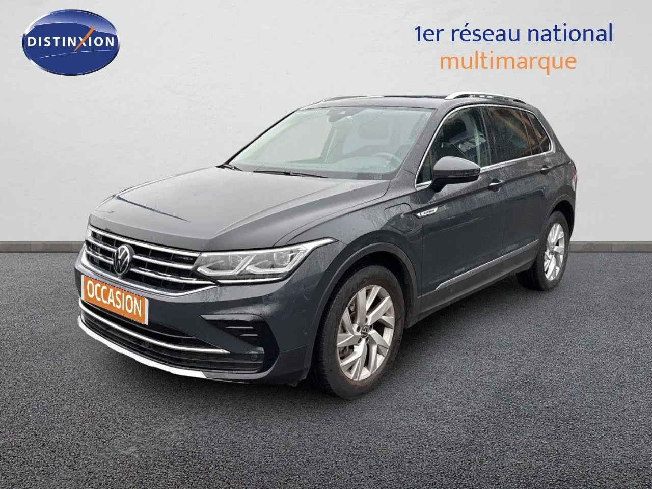 Volkswagen Tiguan 1.4 E-Hybrid gris lunaire en 3/4 avant droit sur sol gris devant un mur blanc.