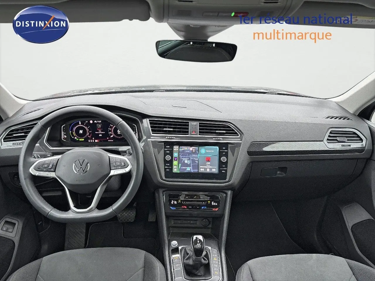 Vue intérieure avant du Volkswagen Tiguan gris lunaire 2022, tableau de bord moderne avec écran tactile et volant multifonction.