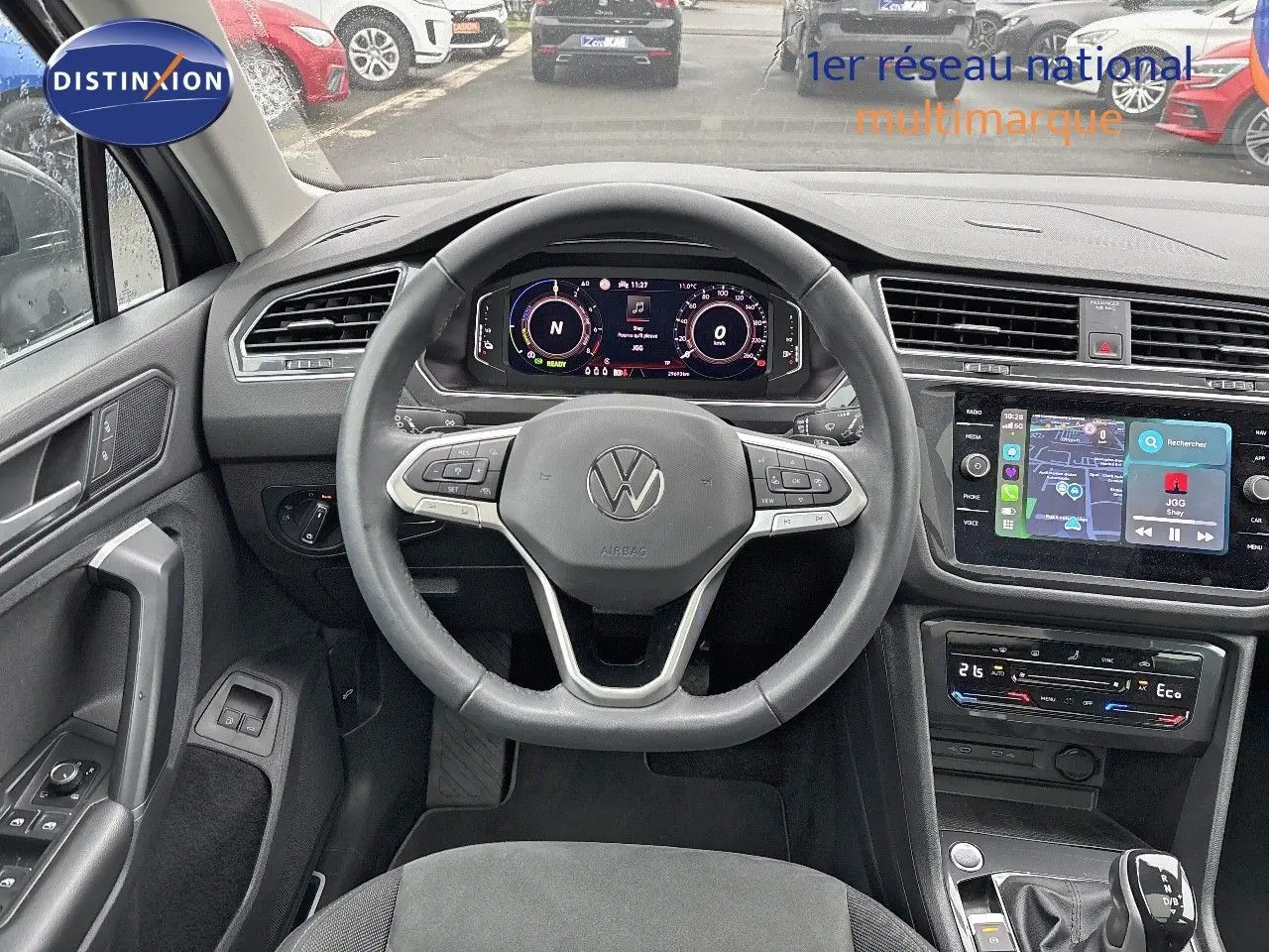 Vue intérieure frontale du tableau de bord et volant du Volkswagen Tiguan 1.4 E-HYBRID gris lunaire avec écran tactile et commandes au volant.