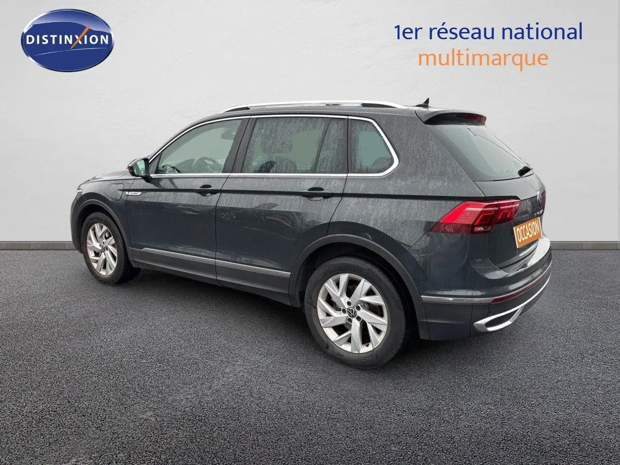 Vue 3/4 arrière côté gauche d'un Volkswagen Tiguan gris lunaire hybride rechargeable de 2022 avec jantes alliage.