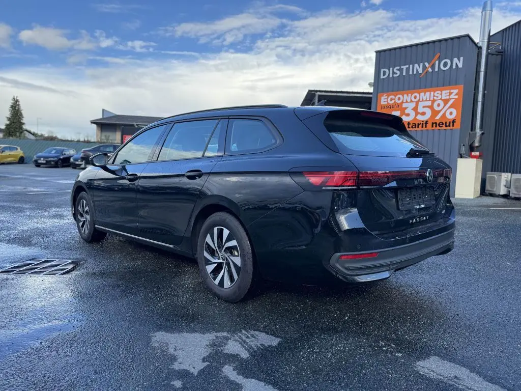 Volkswagen Passat SW noire vue 3/4 arrière droit sur parking humide avec jantes alliage et feux LED.