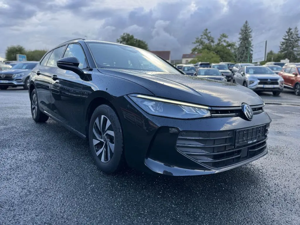 Volkswagen Passat SW noire vue en 3/4 avant gauche, avec phares LED et jantes alliage foncé sur parking humide.