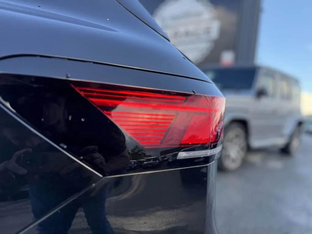 Gros plan sur le feu arrière droit rouge d'une Volkswagen Passat SW noire, finition Life Plus, avec reflet flou d'un autre véhicule en arrière-plan.