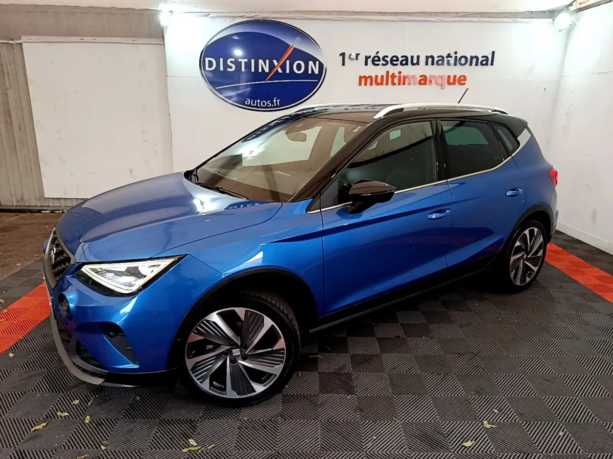 Vue 3/4 avant droite d’un SEAT Arona bleu 2022 avec toit noir et jantes alliage distinctives dans un showroom.