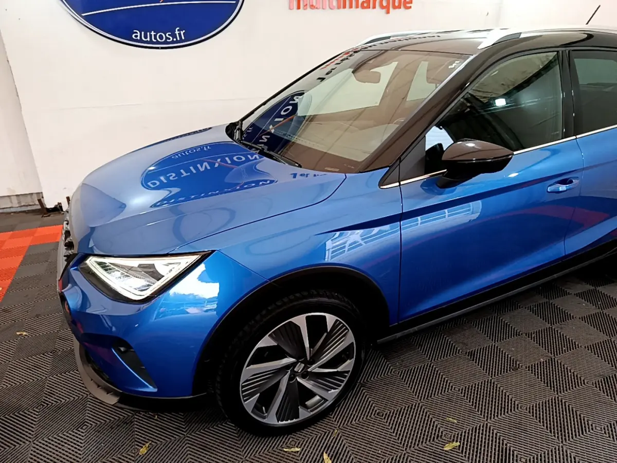 Vue 3/4 avant gauche d'une SEAT Arona bleu métallisé avec jantes alliage et rétroviseur noir.