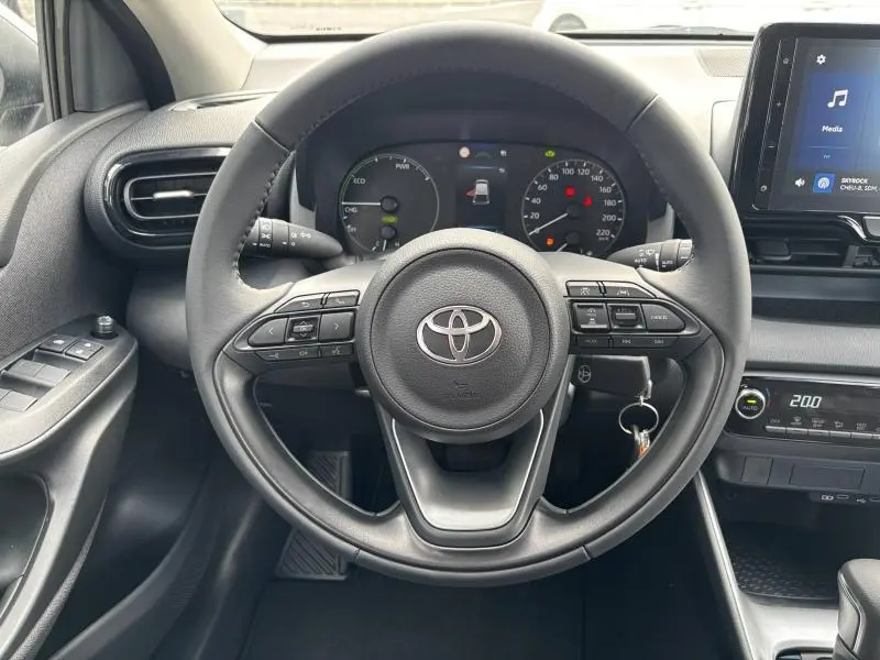 Vue centrée sur le volant et le tableau de bord de la Toyota Yaris 116h Dynamic blanche 2025 avec affichage hybride et commandes au volant.