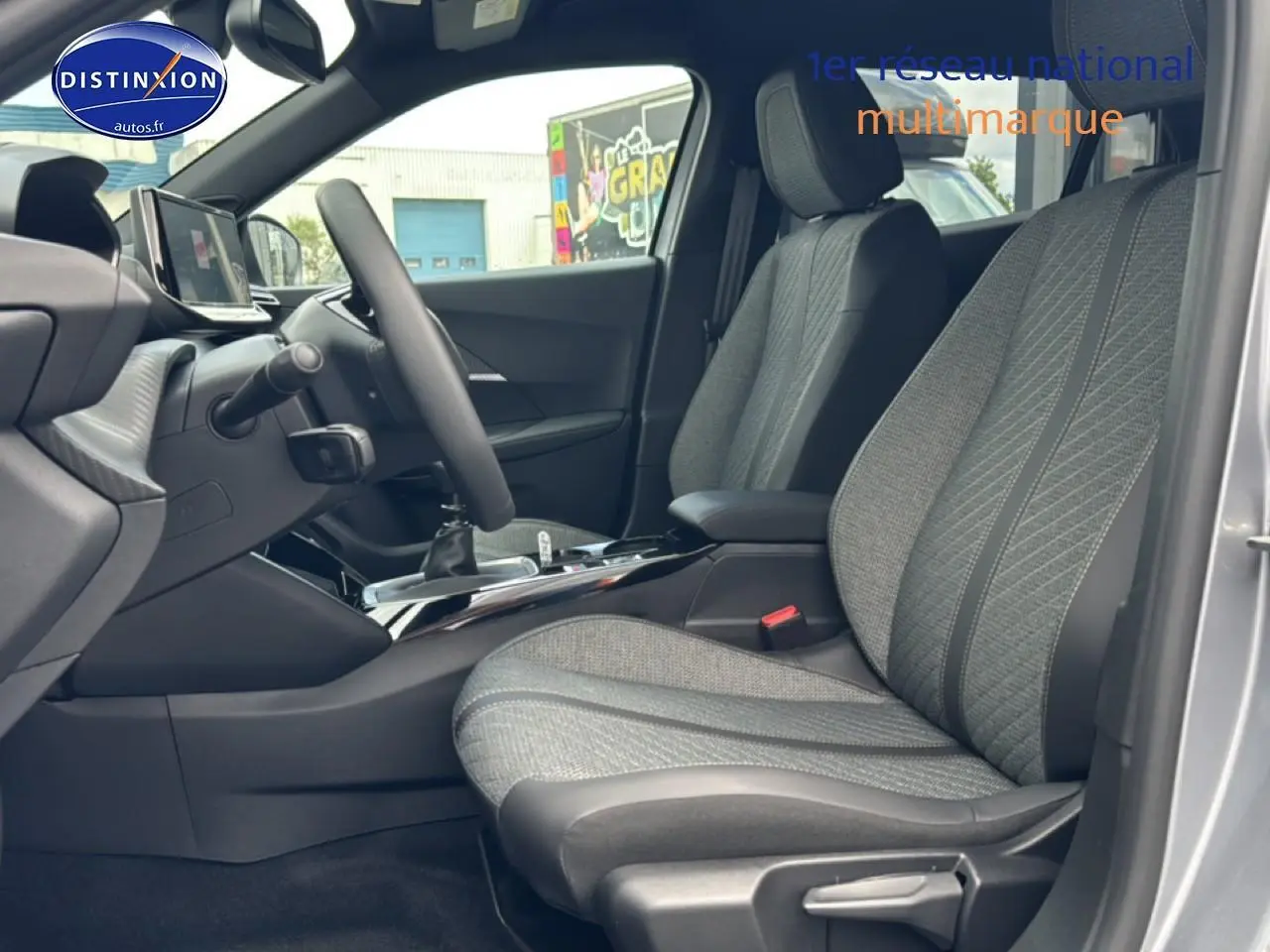Vue intérieure côté conducteur du Peugeot 2008 gris artense, mettant en valeur les sièges en tissu embossé et la console centrale.