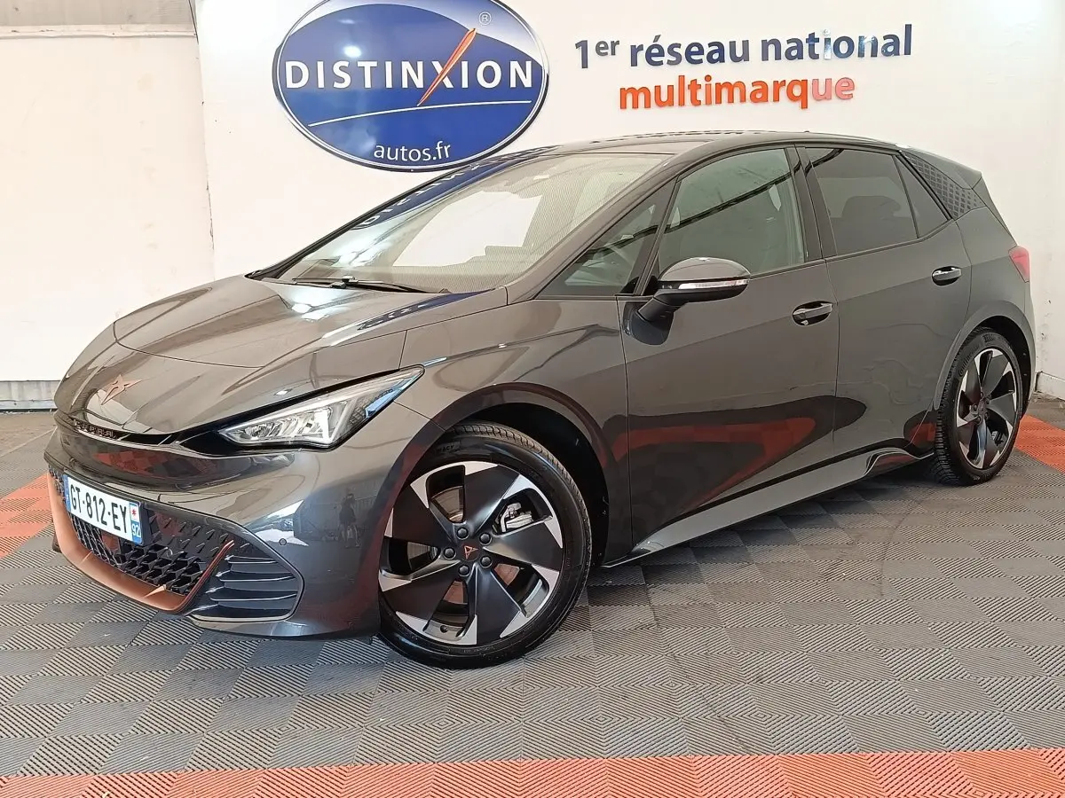 Vue 3/4 avant droite d'une CUPRA BORN gris foncé avec jantes noires et détails cuivrés, stationnée en intérieur showroom.