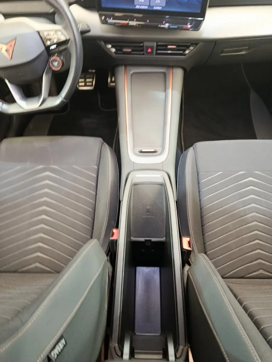 Vue plongeante sur l’intérieur avant du CUPRA BORN gris foncé, montrant la console centrale avec recharge par induction et sièges tissu.