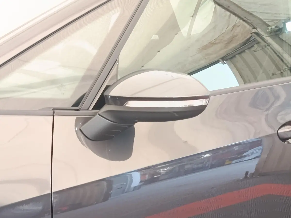 Gros plan sur le rétroviseur côté gauche d'une CUPRA BORN gris foncé, avec reflet sur la portière.