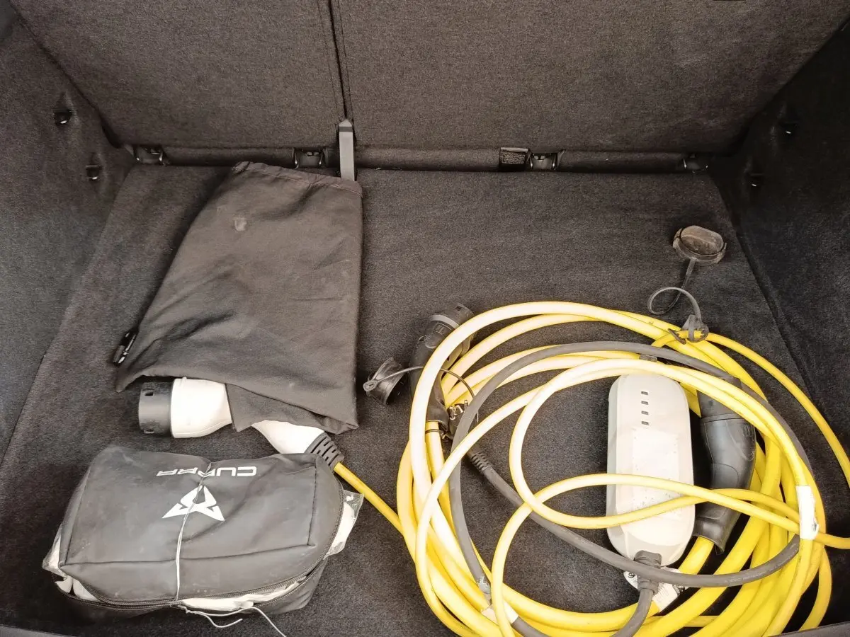 Coffre ouvert d’une CUPRA BORN gris foncé, montrant un câble de recharge électrique jaune enroulé et une housse noire.