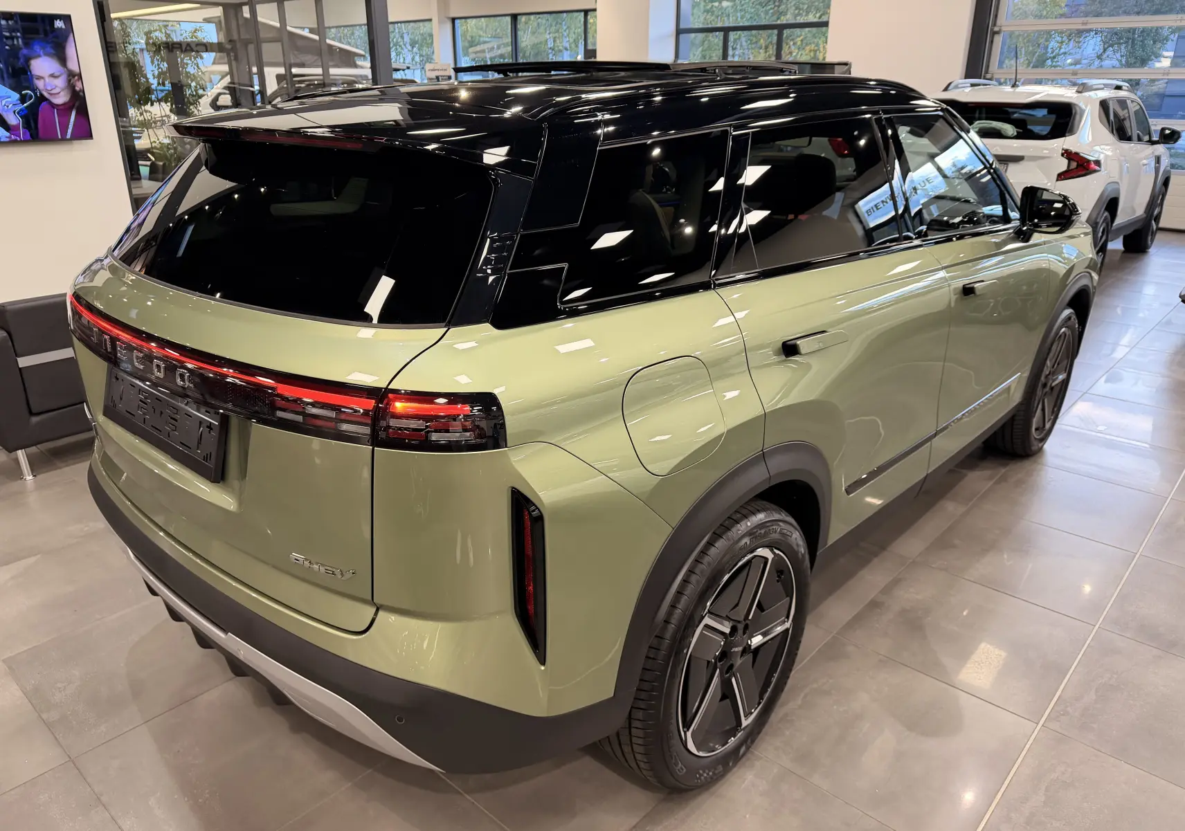 Vue 3/4 arrière droite du SUV JAECOO J7 hybride rechargeable en gris olive avec toit noir brillant en showroom.