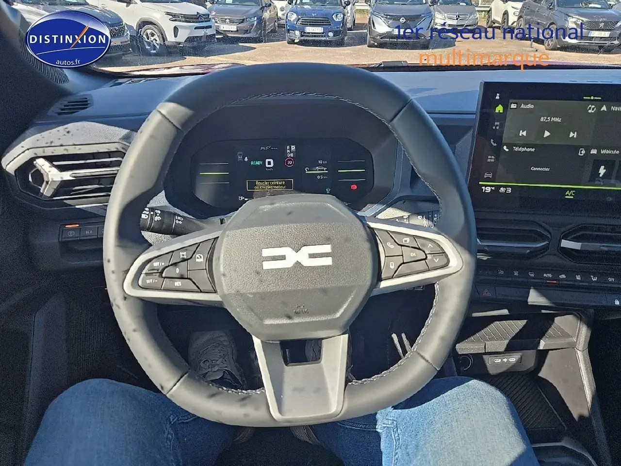 Vue intérieure centrée sur le volant multifonction du Dacia Duster 2025, avec tableau de bord numérique et écran tactile.