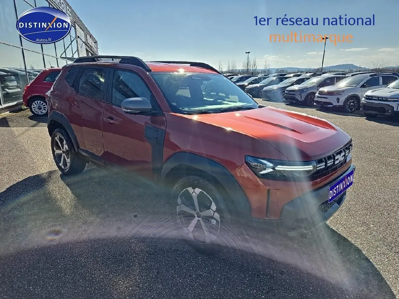 Dacia Duster brun terracotta vu en 3/4 avant droit avec barres de toit et jantes alu distinctives.