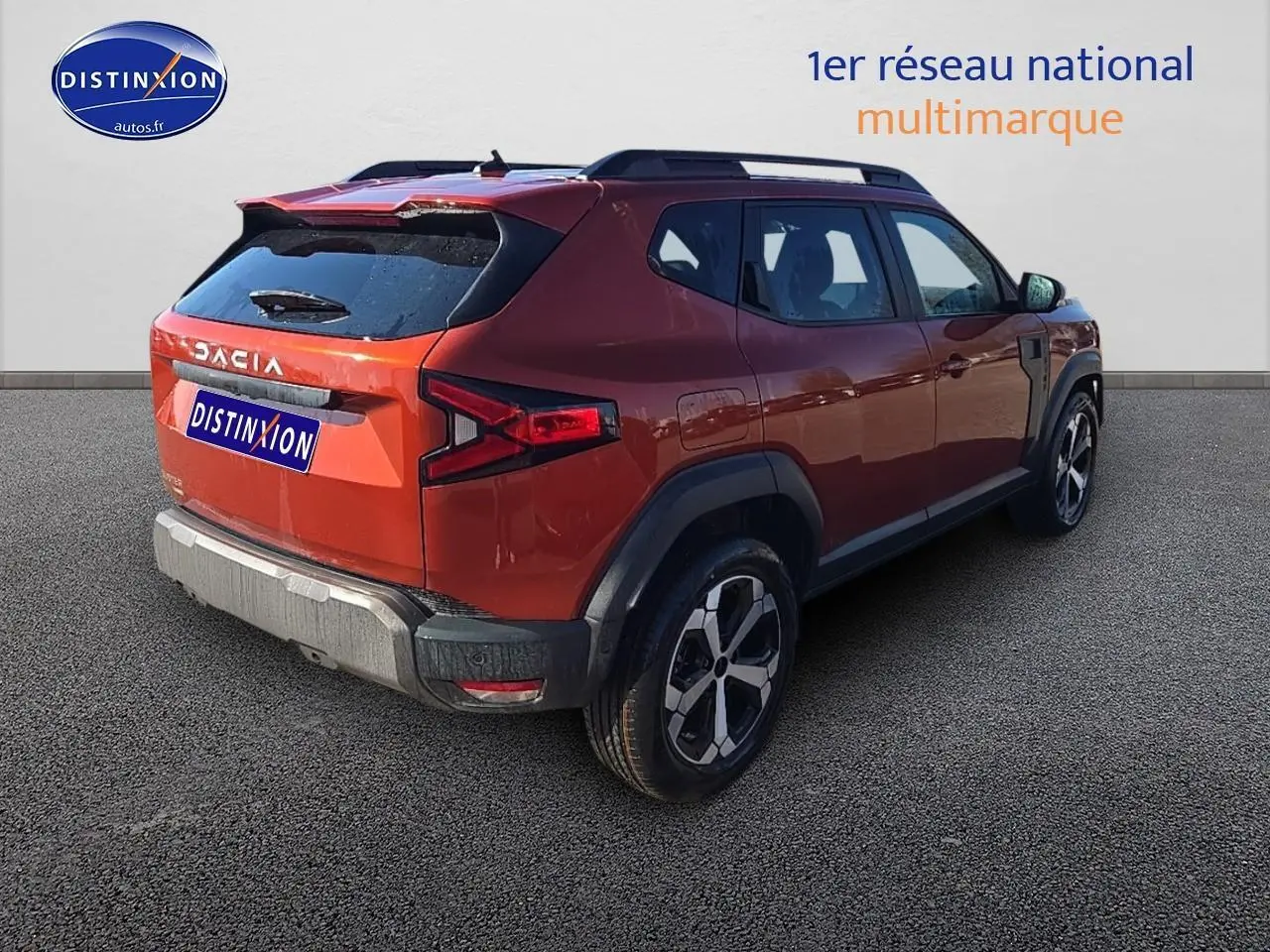 Vue 3/4 arrière droite du Dacia Duster 2025 brun terracotta avec barres de toit et jantes alu distinctives.