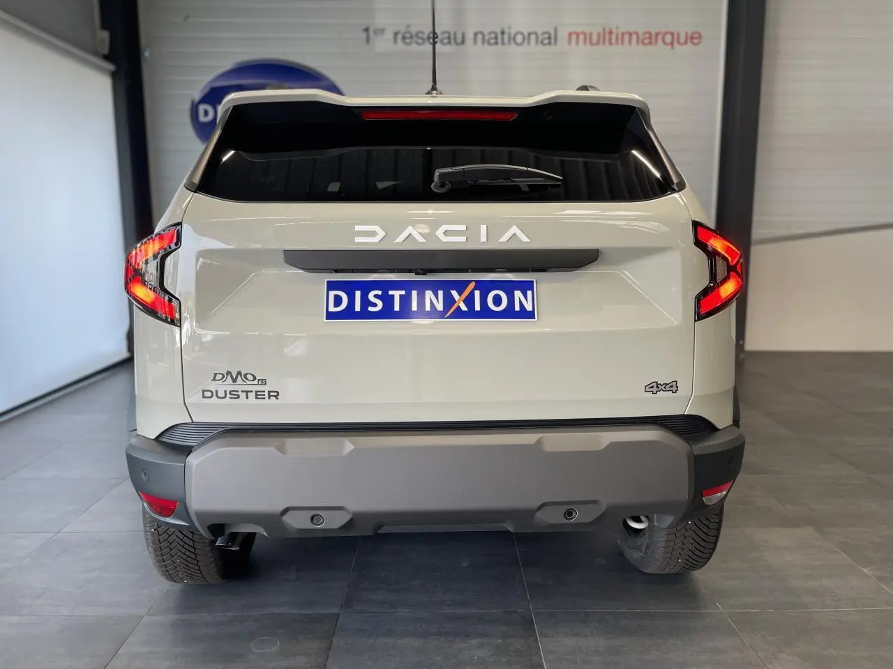 Vue arrière d'un Dacia Duster beige 2025 avec logo DACIA lumineux et badge 4x4 visible sur le hayon.